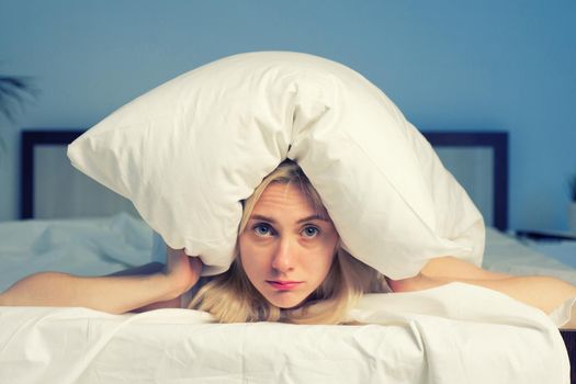 Female lying on bed and closing her ears with pillow - image toned