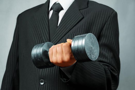 Unrecognizable strong businessman in a suit holds metal dumbbell