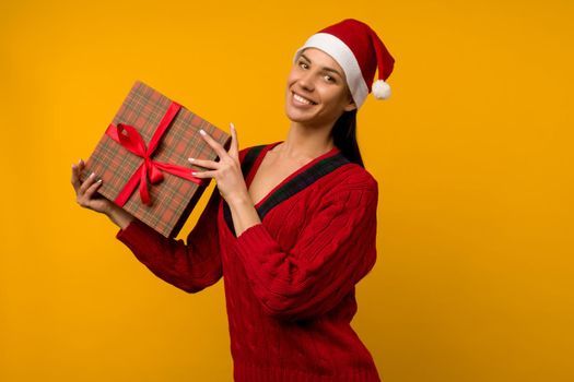 Happy excited young woman in santa claus hat with gift box over yellow background - image