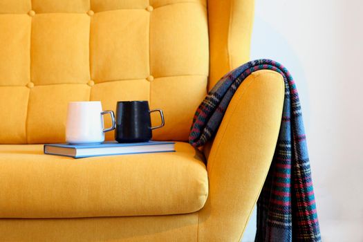 Cup of tea and blue book on a yellow coach with blanket. Still life details in home interior of living room. Cozy home interior, home comfort concept, gender free interior. Modern interior in the room.
