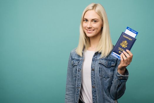 Portrait of a cheerful cute american girl traveller showing passport with tickets isolated over blue background