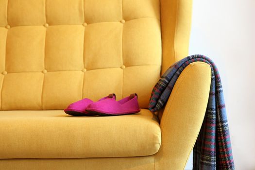 Purple slippers and blanket on a yellow coach. Still life details in home interior of living room. Cozy home interior, home comfort concept, gender free interior. Modern interior in the living room