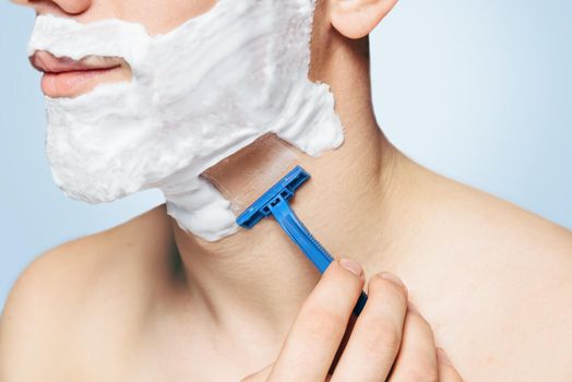 Unrecognizable man with foam on his face is shaving with razor