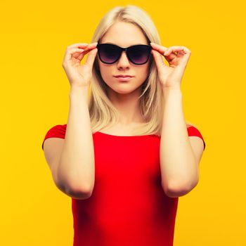 pretty blond lifeguard in red swimsuit and sunglasses on yellow background - image toned