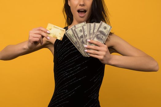 Photo of pleased happy young woman posing isolated over yellow wall background holding money and credit or debt card. - image