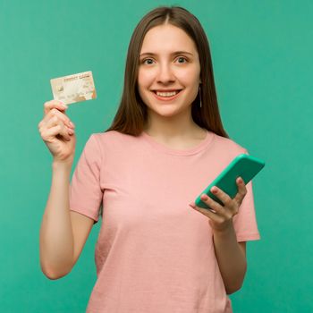 Photo of pleased happy screaming young woman posing isolated over blue wall background using mobile phone holding credit card. - image