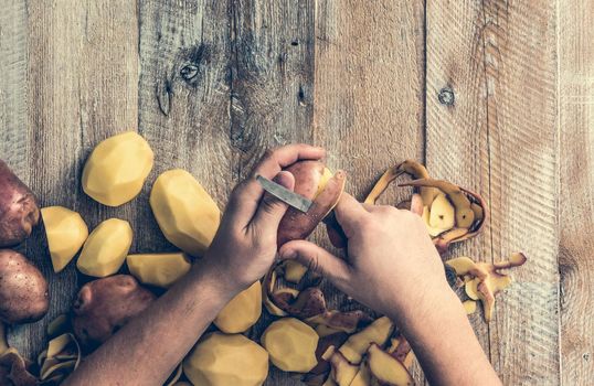 hands peeling potato on wooden board
