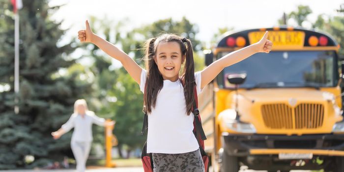 Kids student running into mother's hands to hug her after back to school near the school bus