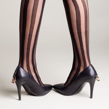 Woman in striped tights black high heel shoes with a padlock posing on a gray background. - image