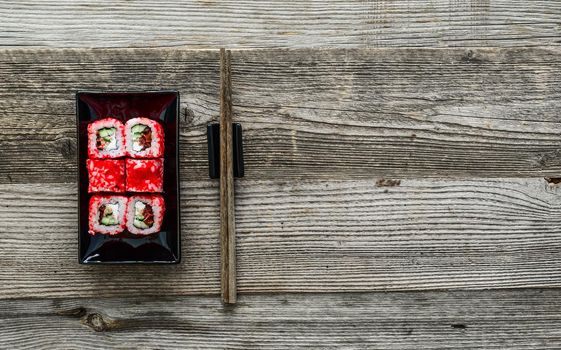 sushi on square black plate with chopsticks on wooden background