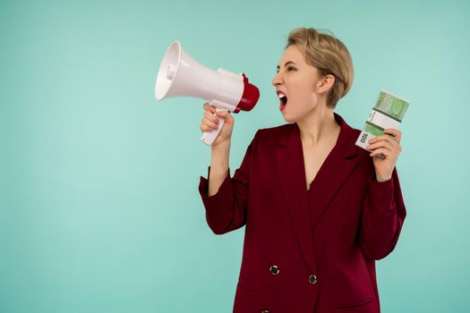 Portrait of beautiful young screaming businesswoman with money and megaphone, on blue background - Image