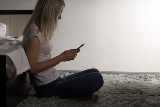 teenager girls sitting on the floor near bad typing on the mobile phone. Young woman suffers from insomnia