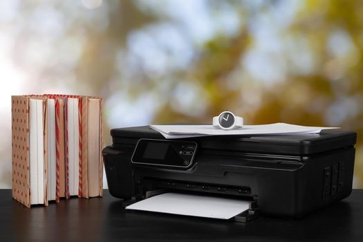 Stack of books and home printer against blurred background, close up