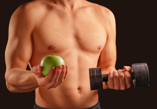 Unrecognizable man holds green apple and dumbbell, concept of healthy life