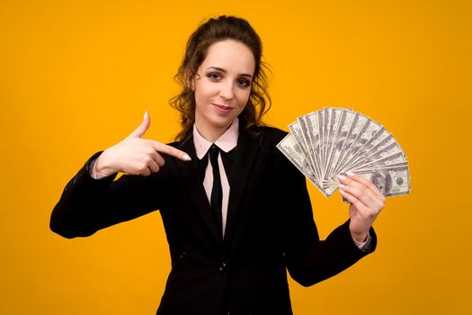 Woman pointing towards a stack of money with her finger isolated on yellow background.