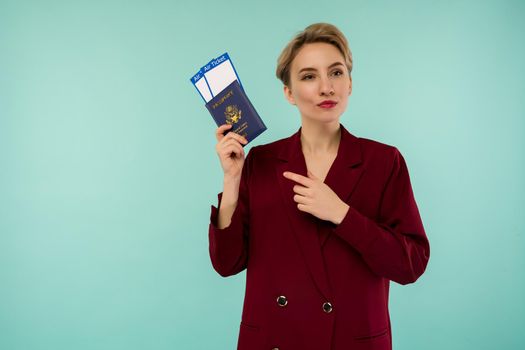 It's time to travel. A modern trendy smiling woman in red suit pointing at air tickets and a passport in her hand.