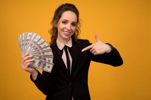 Woman pointing towards a stack of money with her finger isolated on yellow background.