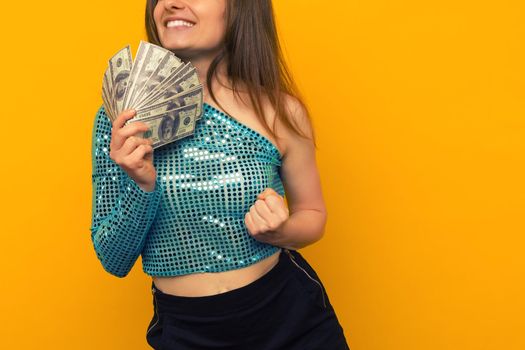 Joyful girl won the lottery and holds a fan of US dollars in her hands on a yellow background - image