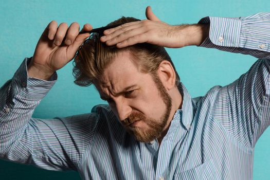 young blond man in striped shirt comb his hair on blue background