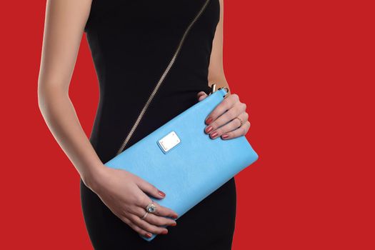 The fashionable young woman in black dress holding blue clutch .Red background