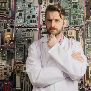 contemplative electronics engineer stands near the wall of motherboards.