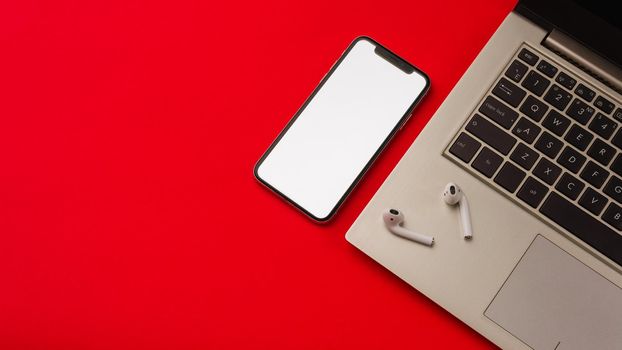 Tula, Russia - May 24,2019: Apple iPhone X and Airpods on red background with notebook. The screen of the smartphone is white. Mockup.