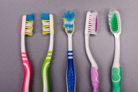 Five Old colorful toothbrushes on gray background.