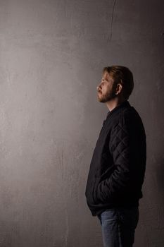 An emotionless portrait of a man in a black jacket and jeans standing near a wall. copy space. deadpan without retouching