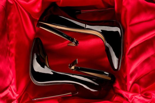 Black fetish shiny patent leather stiletto high heels with ankle strap on red satin background