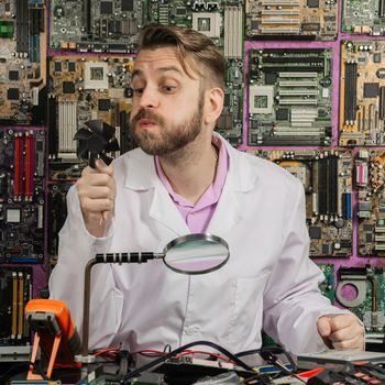 A young funny electronics engineer blowing on a computer fansitting at his lab table