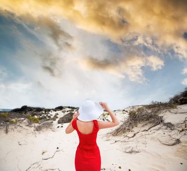beautiful young woman in evening red dress and white hat on a background of a sand desert