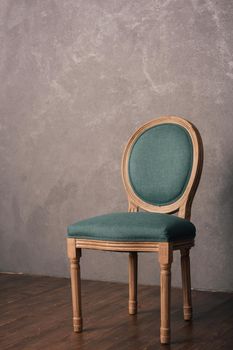 Green luxurious vintage chair stands on a dark wooden floor.