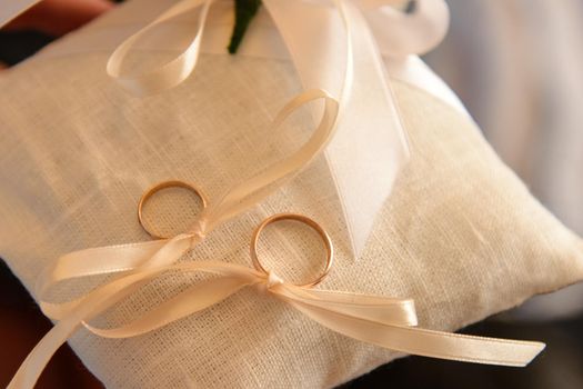 two wedding rings on a cushion tied with ribbon.