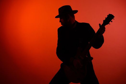 silhouette of a guitarist in a hat on a red background.