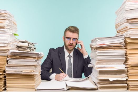 Business executive talking on the phone working in the office and piles of paperwork, he is overloaded with work - image