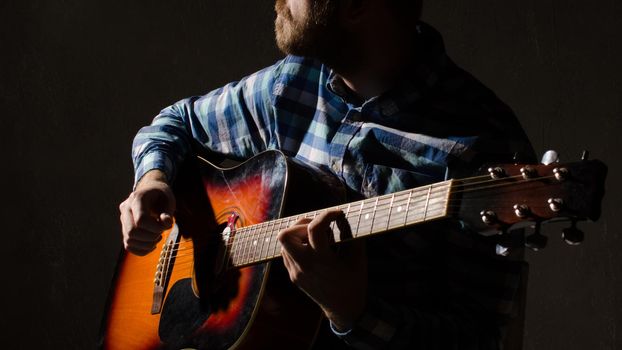 A bearded man in a plaid shirt plays an acoustic guitar. hands close-up.