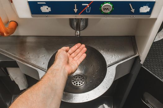 The guy brings his hand to the automatic water supply tap in the modern toilet of the stadler electric train.