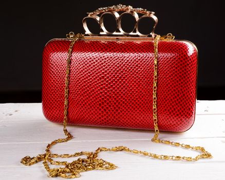 Red hand bag clutch with pen brass knuckle on black background.