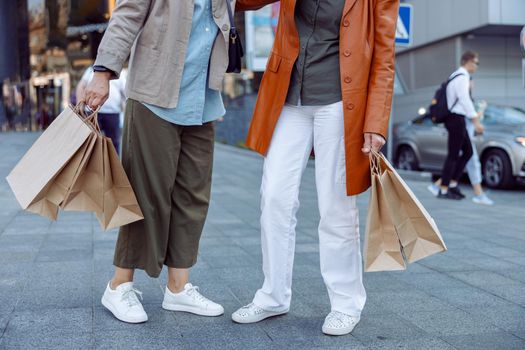 Pair of senior ladies holds shopping bags standing on modern city street on autumn day closeup. Friends spend time together