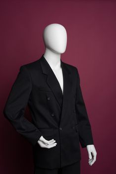 White male mannequin in a black business suit on a ruby background - image