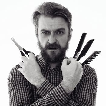 serious bearded hairdresser holding scissors and a comb. association with a person waving a marvel