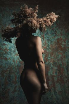 naked girl in a hat of spikelets standing in studio at color wall