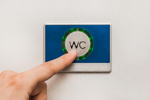 A man's hand presses a finger on the flush button in a modern toilet of the stadler electric train, close-up.