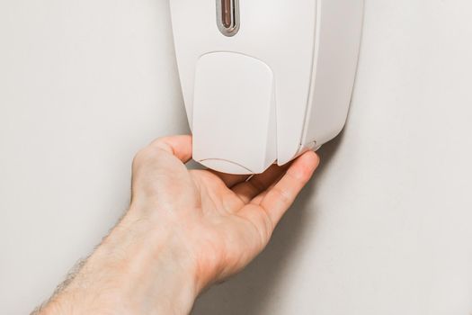 The man raised his hand to the soap dispenser, close up.