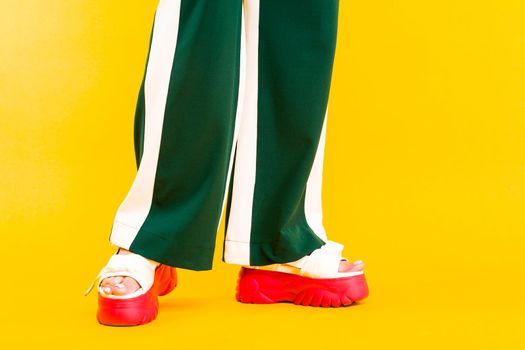Women's legs in sport sandals with red soles and green pants with stripes on a yellow background.