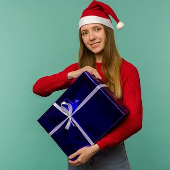 Happy excited young woman in santa claus hat with gift box over blue background - image