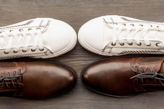 Men's classic brown shoes and white sneakers on a wooden background. Top view - image