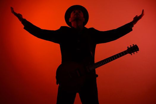 guitarist in a hat is standing with his arms outstretched on a red background