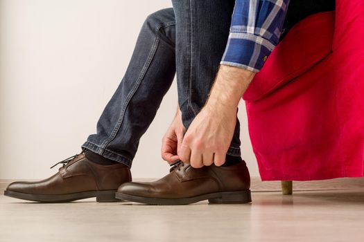 A man in a stylish brown shoes, tying laces is sitting on a red chair - image