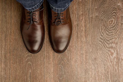 The man wears brown classic shoes on wooden flour. - image